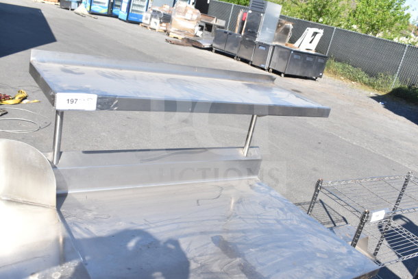 Commercial stainless steel table with over shelf and under shelf, minor surface marks, tag number 197 visible.