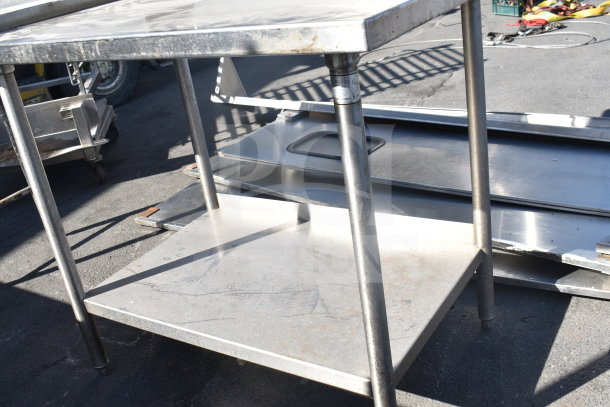 Stainless steel commercial table with over shelf and under shelf, showing signs of wear and surface scratches.