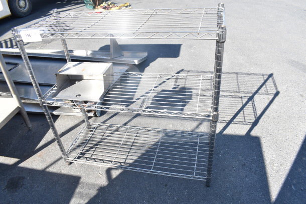 Chrome finish 3-tier wire shelving unit on pavement. In good condition. Buyer must dismantle; consider freight charges.