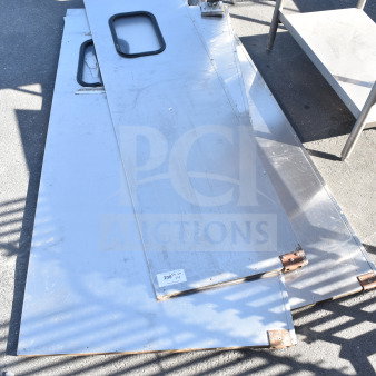 Three metal swinging kitchen/traffic doors, used, with built-in windows and visible hardware, stacked outdoors.
