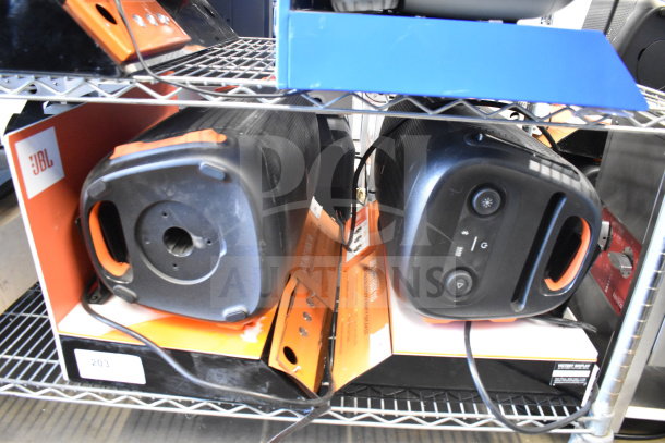 Two JBL PartyBox portable Bluetooth speakers on a shelf, showcasing front controls and brand packaging. Condition appears good.