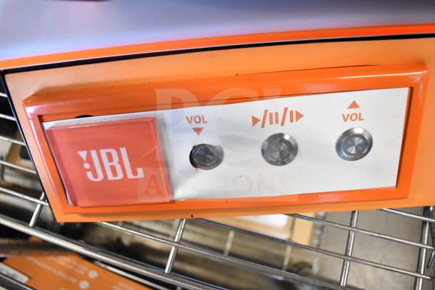 JBL PartyBox speaker control panel with volume and playback buttons. Orange trim, JBL logo visible.
