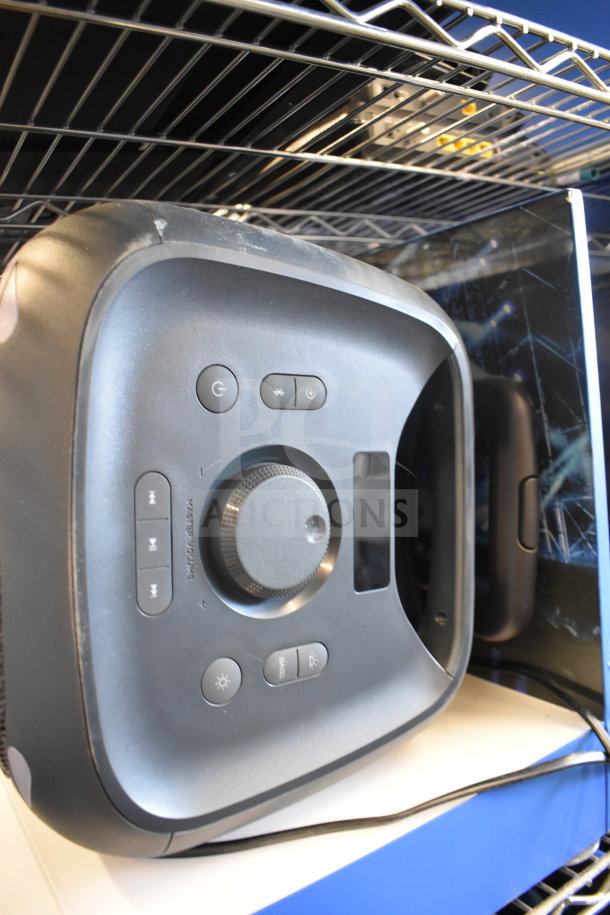 Onn portable Bluetooth speaker on shelf, featuring control buttons and volume knob. Visible light signs of wear.