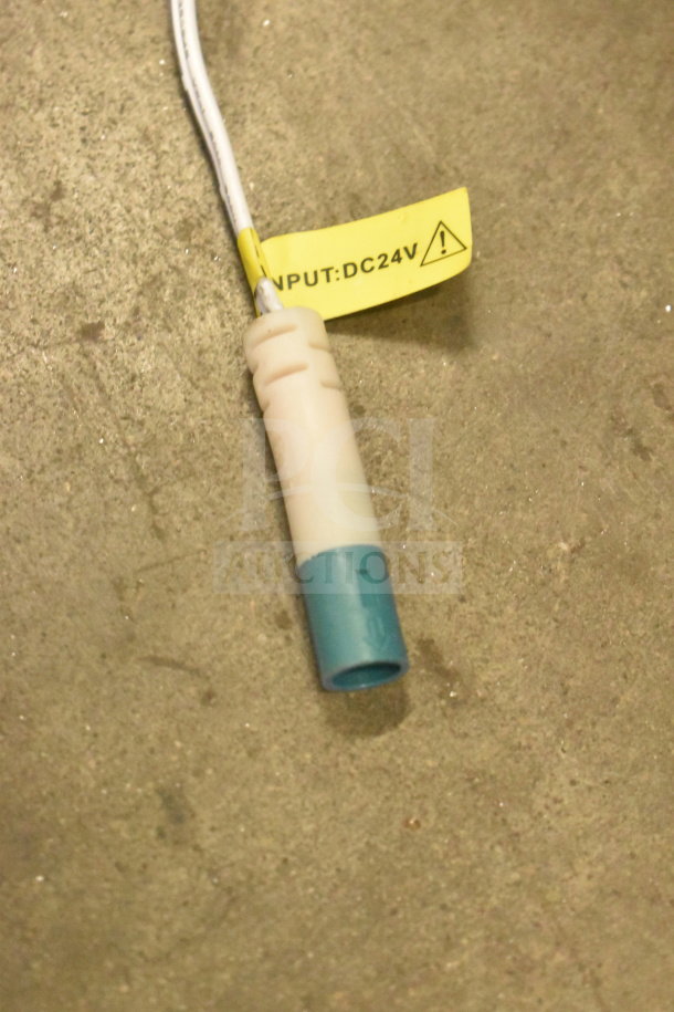 Close-up of a white and blue electrical connector with a yellow tag reading "INPUT: DC24V" on a gray surface.