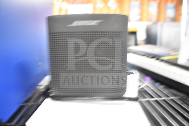 Bose speaker in good condition, black with mesh front. Part of an auction lot with multiple items including a Netgear router.