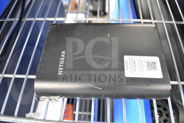 Black Netgear router with visible branding and label indicating model "Netgear 62," on a wire shelf. Showing wear.