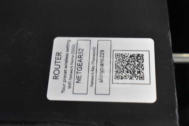 Netgear router label showing WiFi SSID "NETGEAR52" and password "shinypiano229" with QR code.