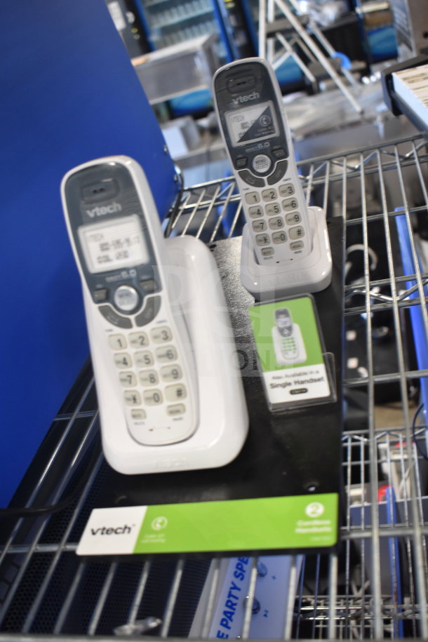 Two Vtech cordless phones with charging bases, displayed on a metal shelf. Visible labels indicate DECT 6.0 technology.