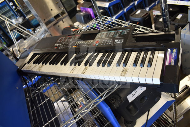 Electronic keyboard with various controls and keys, showing signs of wear, placed on a metal shelf. Tags and labels visible.