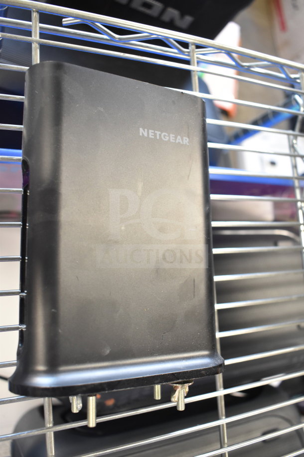 Netgear router, black, in good condition, with visible power and Ethernet ports, set on a metal shelf.