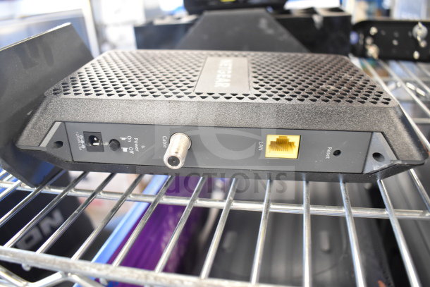 Netgear router with LAN and cable ports, power switch, on metal shelf. Condition appears used, branding visible.