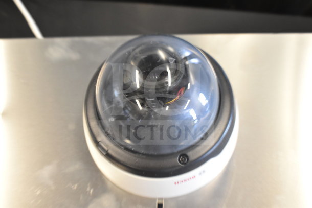 Dome security camera with clear casing, compact design, and visible wiring. Brand label partially visible, in good condition.