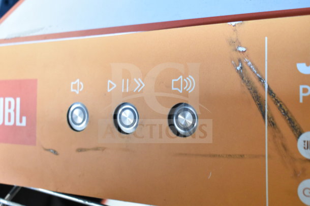 JBL Boombox 3 control panel with volume and playback buttons, visible wear marks, orange casing.