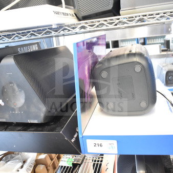 Samsung and Onn speakers, good condition. Samsung has control panel, Onn is a medium party speaker. Auction tag reads "216."
