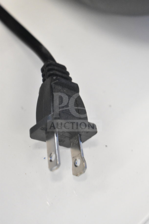 Close-up of a two-prong power plug, possibly for a Samsung Speaker or Onn Medium Party Speaker, resting on a white surface.
