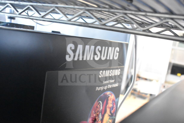 Samsung Sound Tower speaker in box with "Pump up the music" label under metal shelf.