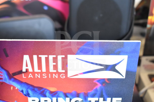 Altec Lansing IMT7002 speaker with promotional packaging, logo visible. Background suggests additional speakers.