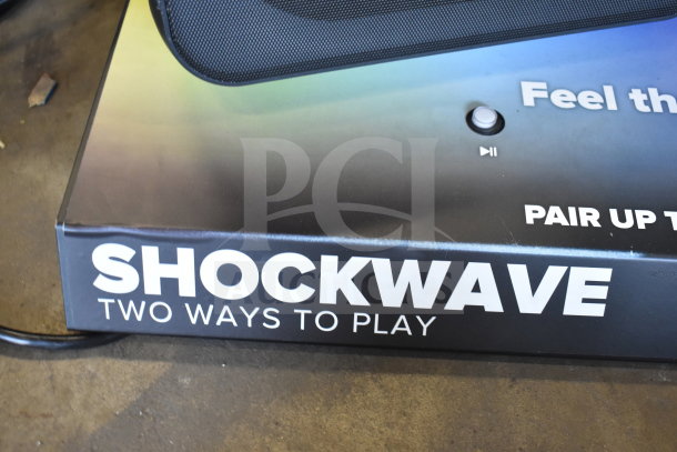 Store display with "SHOCKWAVE Two Ways to Play" branding, featuring two integrated speakers and control buttons.