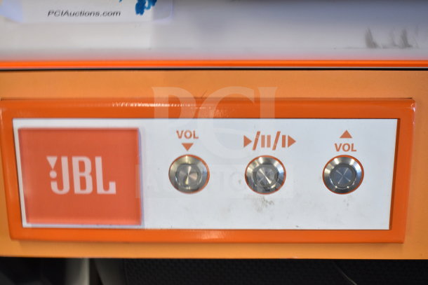 JBL speaker display panel with orange border, featuring volume and play/pause buttons.