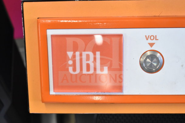 JBL speaker display with orange branding and volume control button, indicating premium audio quality.