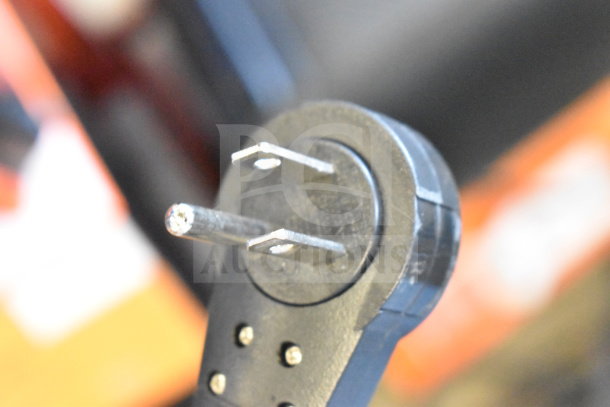 Close-up of a black electrical plug with metal prongs, part of a store display featuring JBL speakers.
