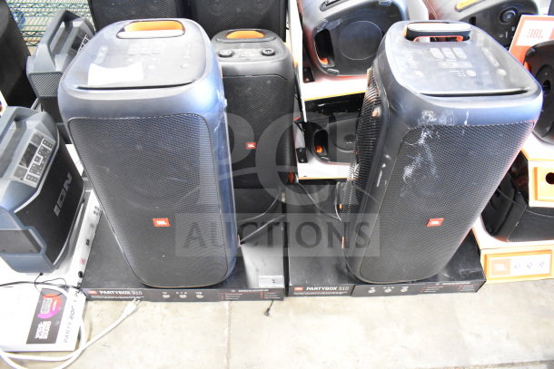 Two JBL Partybox 310 speakers on store display, visible wear, cables connected, marked boxes below each speaker.