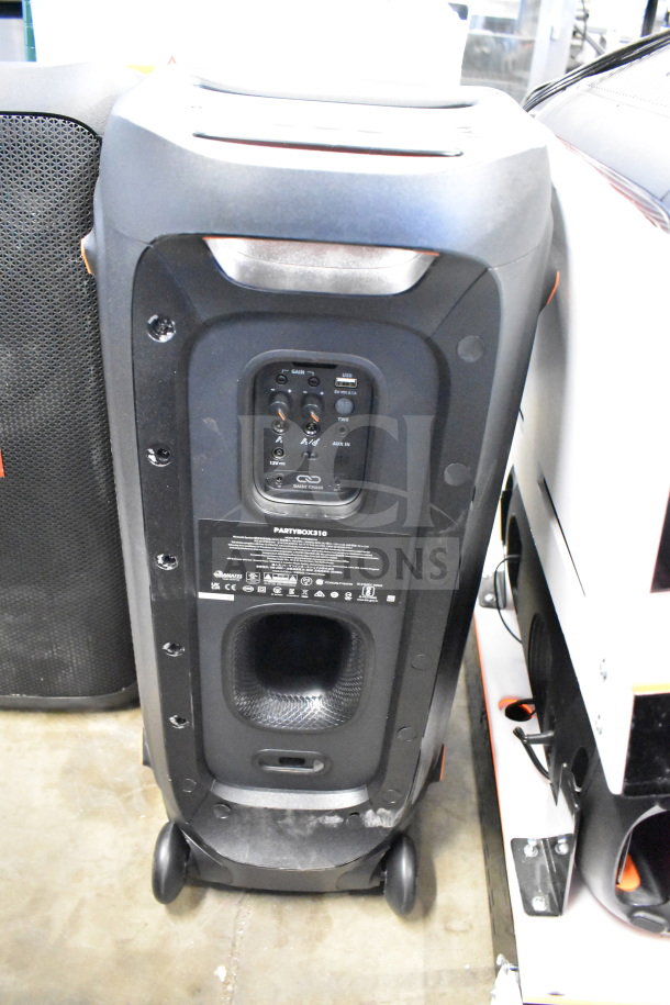 Two JBL Partybox 310 speakers, featuring connectivity ports and controls panel, on wheels for mobility; model label visible.