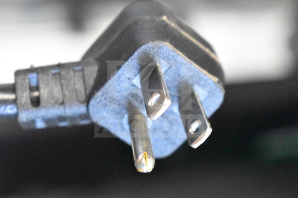 Close-up of a three-prong electrical plug. Black rubber casing, metal prongs slightly worn. Used condition.