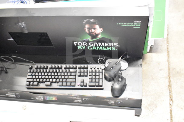 Gaming store display with Razer keyboard, headsets, and mouse. Features "For Gamers. By Gamers." branding.