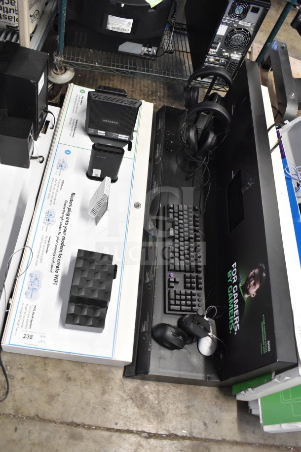 Store display featuring Netgear routers, gaming keyboard, and headphones. New condition, ideal for tech enthusiasts.
