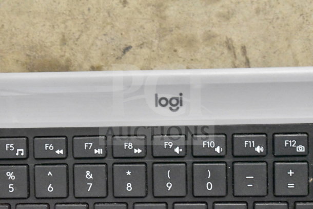 Logitech keyboard, black keys with media controls, visible "logi" logo, part of a mixed office electronics lot.