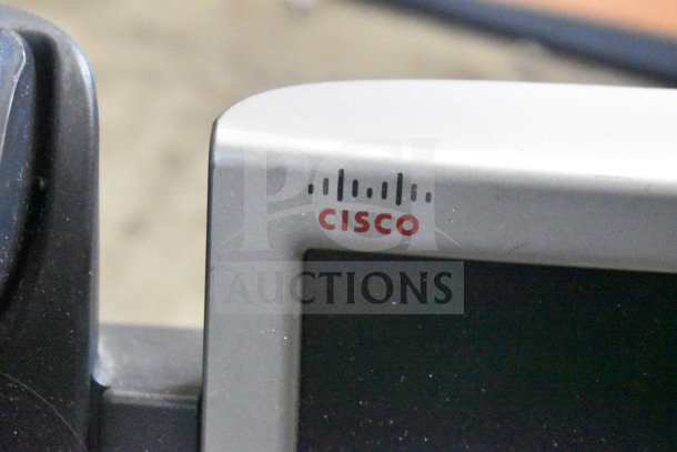 Lot of office electronics including Cisco corded phones, a keyboard, and a credit card reader. Visible Cisco logo.