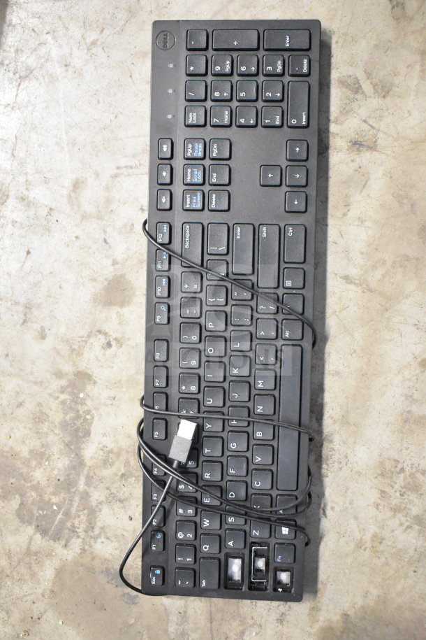 Dell corded keyboard with USB connection shown on concrete surface; moderate wear visible. Part of mixed office items lot.