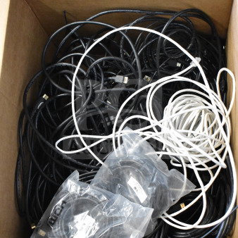 Lot of cables in a cardboard box, with mixed black and white wires. Includes cables in plastic packaging, some labeled.
