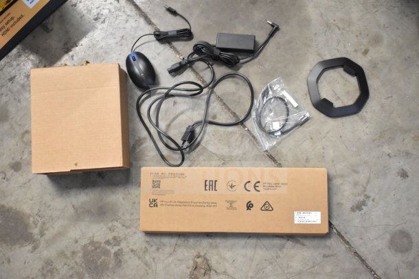 HP computer mouse, keyboard in box, power cables, and stand on concrete floor. Labels show regulatory info and UKCA markings.