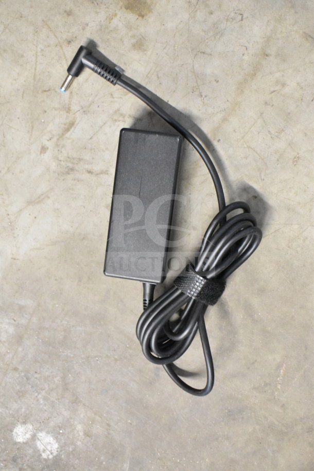 Black power adapter with attached cable on concrete surface, coiled and secured with a Velcro strap.