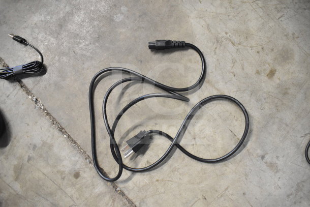 Black power and audio cables on a concrete floor, one with a three-prong plug, in good condition.