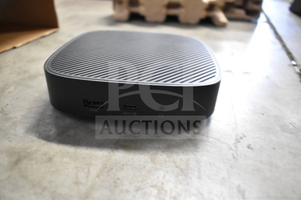 Small black device with a textured top, featuring USB and audio ports. Appears in good condition.
