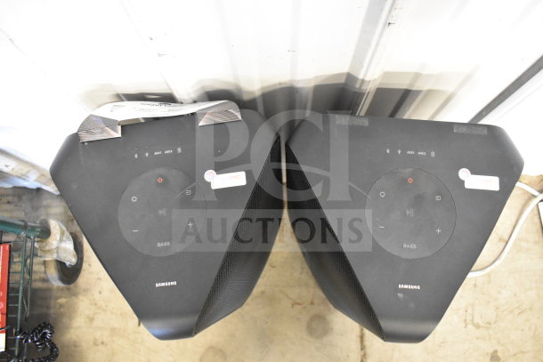 Two Samsung speakers, triangular shape, with control interfaces and "Play Demo" stickers. Used as store displays.