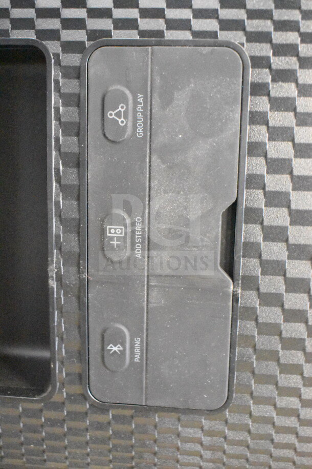 Onn speaker control panel showing buttons for group play, stereo addition, and Bluetooth pairing on a checkered surface.