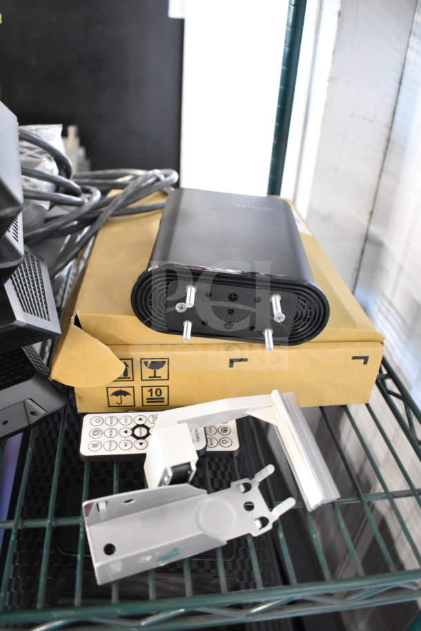 Various electronics and accessories including Netgear router, cables, and mounting brackets on a shelf. Appears unused.