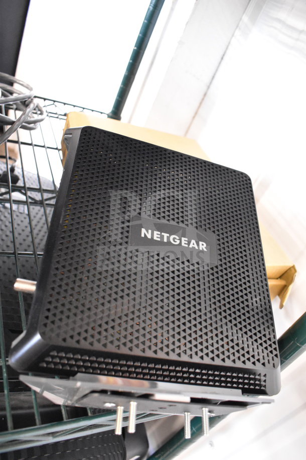 Netgear router on shelf, part of 20-item auction lot. Black, perforated design, visible Netgear logo.