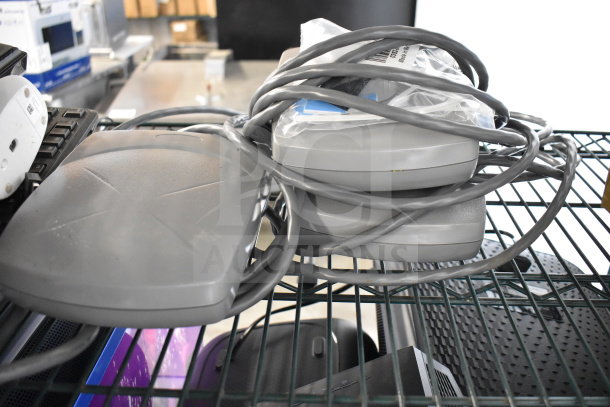 A collection of electronic items including a Netgear router, tangled cables, keyboards, and computer mice on a shelf.