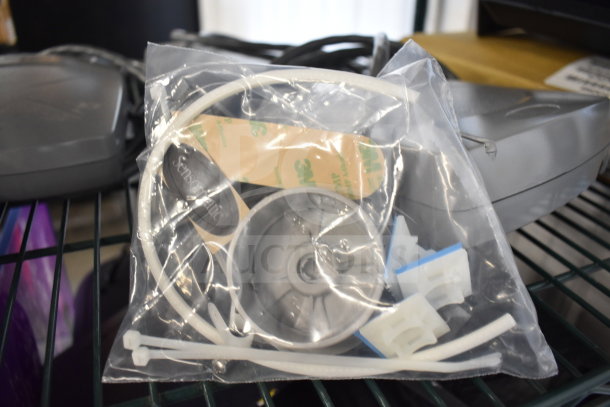 Bag of assorted computer accessories on a shelf, including cable ties, adhesive mounts, and labeled Sensormatic component.