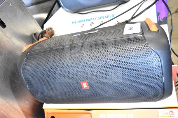 JBL Partybox 110 Bluetooth speaker on store display. Black with orange accents, branded with JBL logo, new condition.