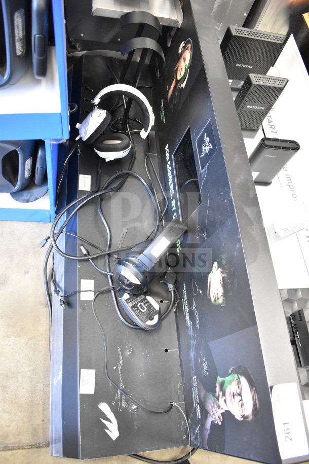 Store display with Netgear routers, Razer branding, two headphones, and cables. Some visible wear.