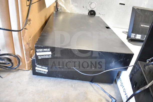 Stack of two black Victory Display units with visible labels, alongside a NETGEAR router. Slight wear visible.