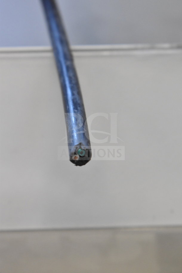 Close-up of a metal cable with visible inner wires. Part of a store display with headphones and monitor setup, details not visible.
