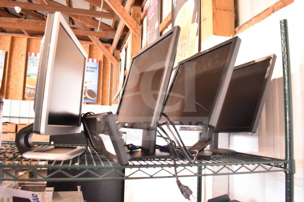Four assorted monitors on a metal shelf, including Dell and HP models, sold as a lot. Various conditions, with visible cables.