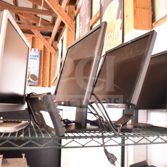 Four assorted monitors on a metal shelf, including Dell and HP models, sold as a lot. Various conditions, with visible cables.